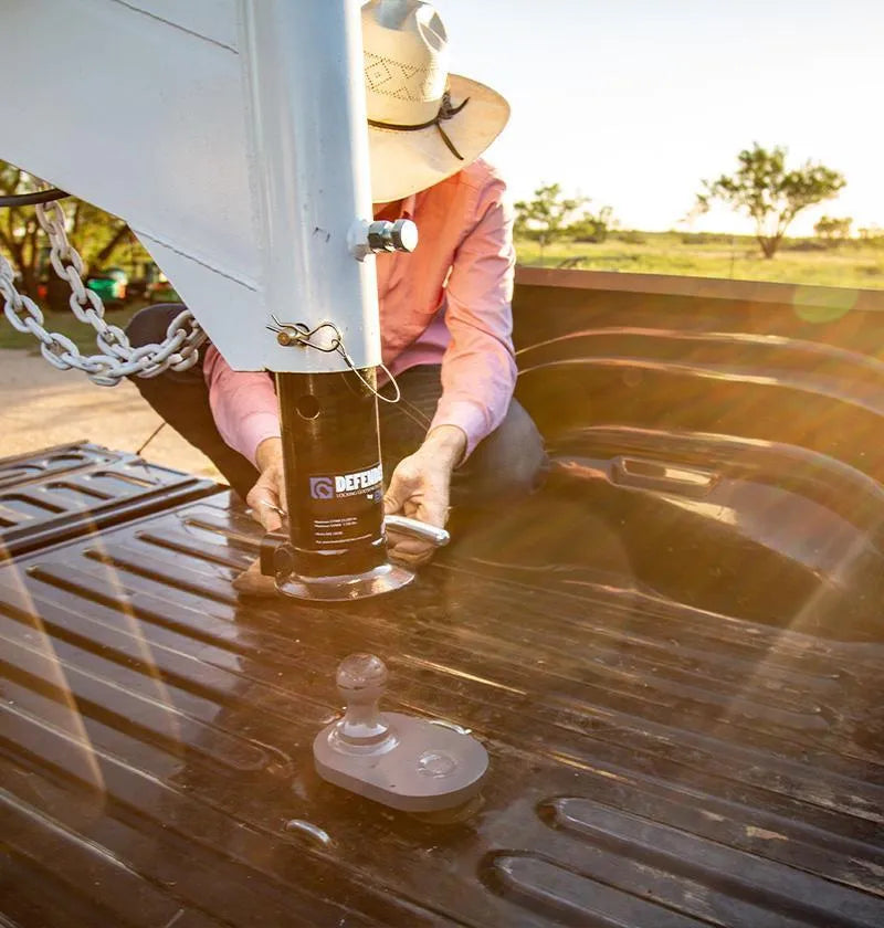 B&W Defender coupler being lowered onto a gooseneck ball in a truck bed, with the ball and its mounting plate visible in the foreground
