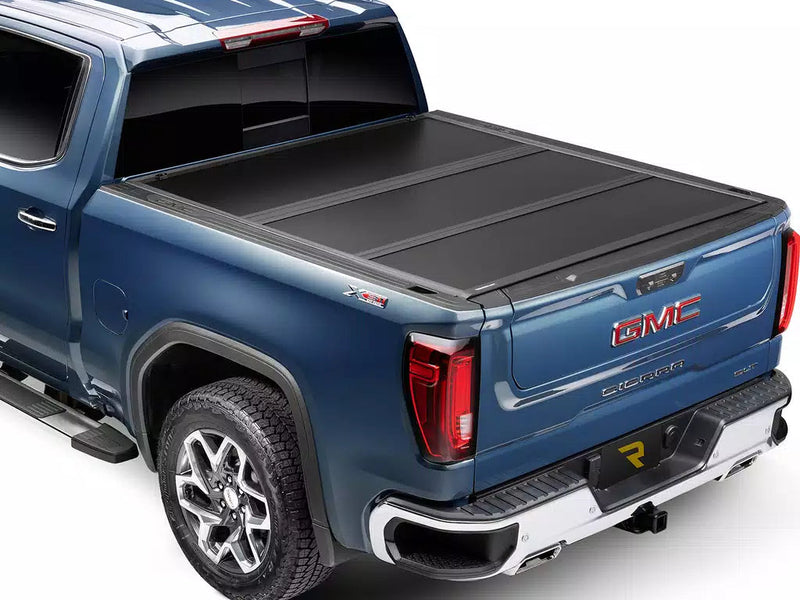 UnderCover Select hard folding tonneau cover closed and flush on a pickup bed, rear three-quarter view, matte-black panels sitting level with the bed rails.