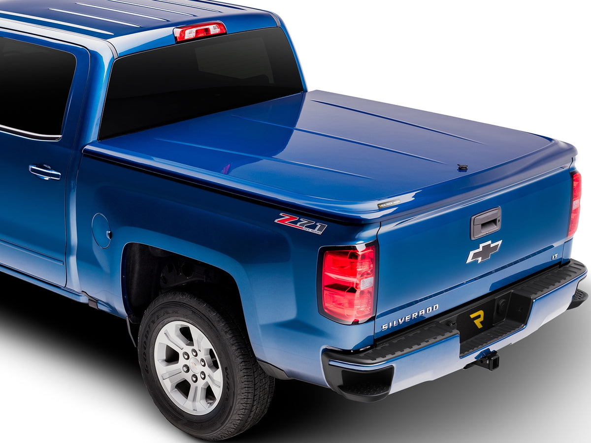 UnderCover LUX one-piece tonneau cover closed and latched on a pickup bed, rear three-quarter studio view, the lid sitting flush across the tailgate with no bed floor showing.