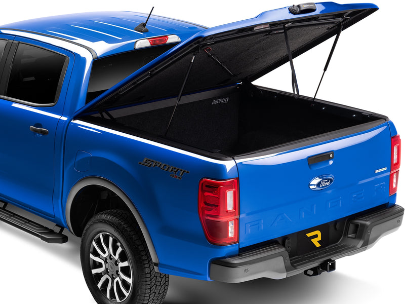 UnderCover Elite LX one-piece tonneau cover raised on its gas struts, rear three-quarter view, the carpeted underside of the lid and the lined bed floor both in frame.