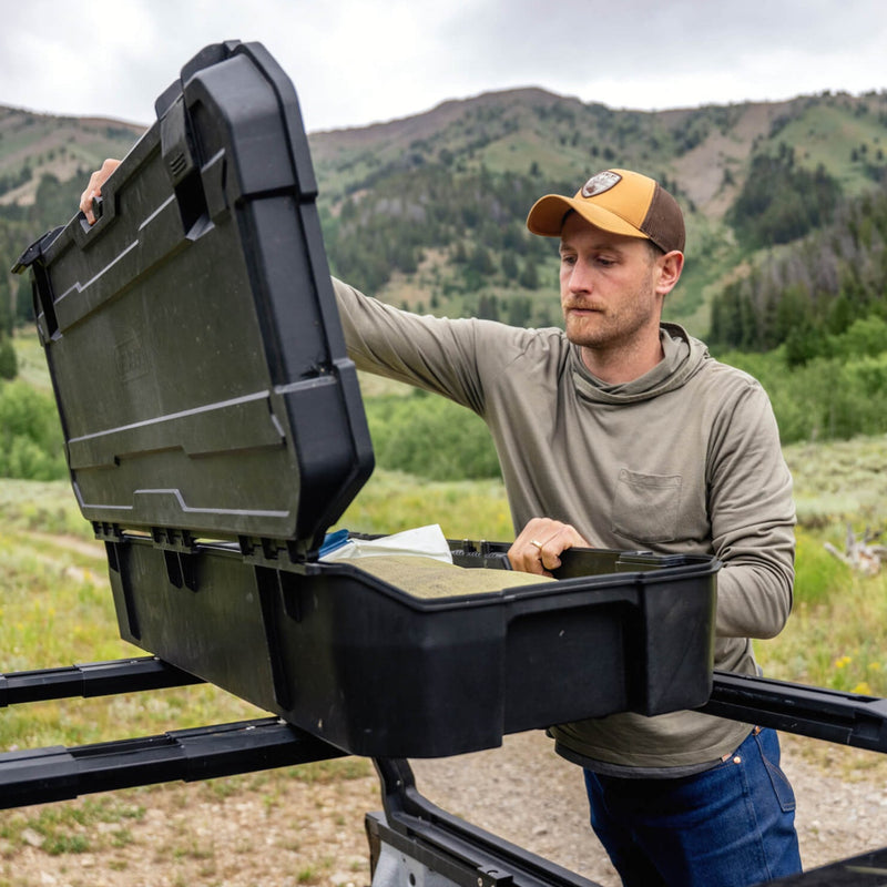Person lifting a black DECKED case off a truck bed rack crossbar in open country