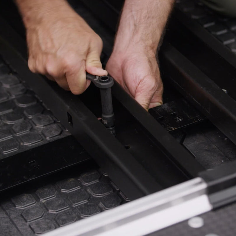 Hands using a ratchet to fasten the black CargoGlide mounting rail down onto a DECKED Drawer System deck