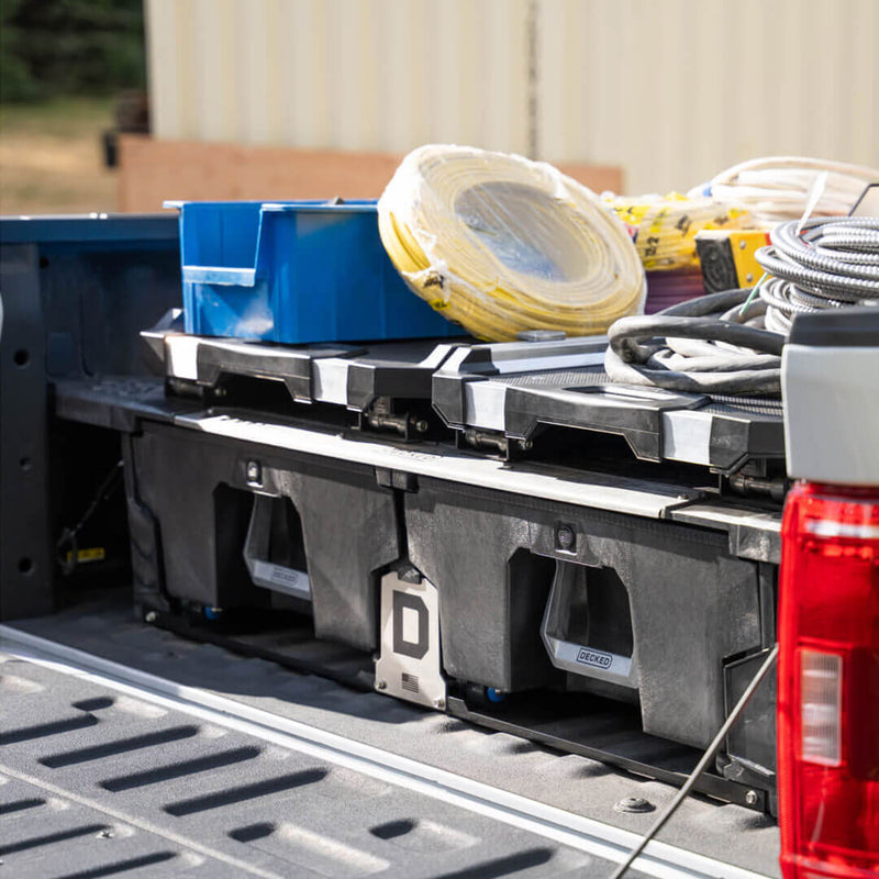 CargoGlide sliding tray mounted above a DECKED Drawer System in a truck bed, loaded with electrical conduit and parts bins, drawers visible underneath