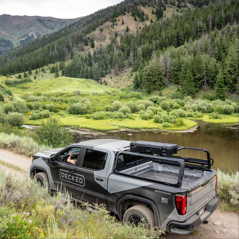 DECKED branded GMC pickup on a mountain track with a black DECKED case mounted on the bed rack crossbars