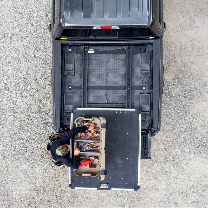 Overhead view of a DECKED Drawer System with a slide-out tray extended over the tailgate and a tan DECKED Honcho 80 case mounted on it, open to hand tools