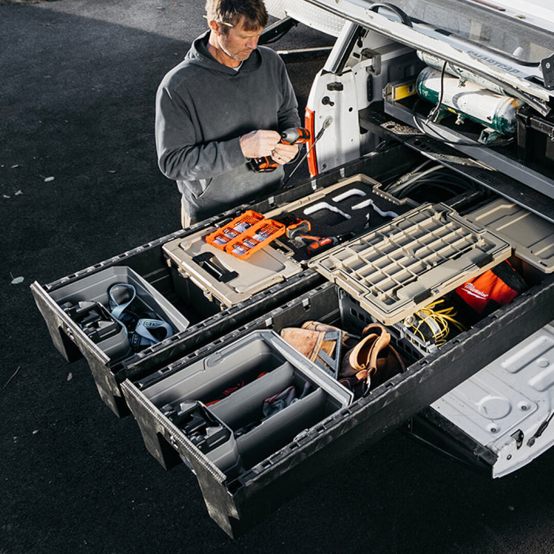 Tradesman working at an open DECKED Drawer System in a white service truck with gray organizer trays in both lower drawers