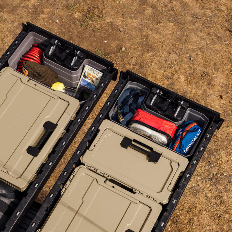 Two open DECKED drawers with gray Drawerganizer trays at the handle ends holding a coiled hose, a trail map and a medical kit alongside tan DECKED cases