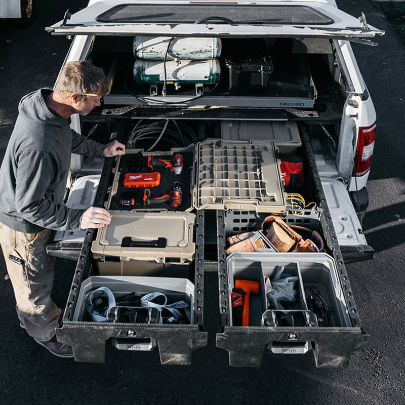 Tradesman at an open DECKED Drawer System in a white pickup with gray organizer trays and DECKED cases filling both drawers