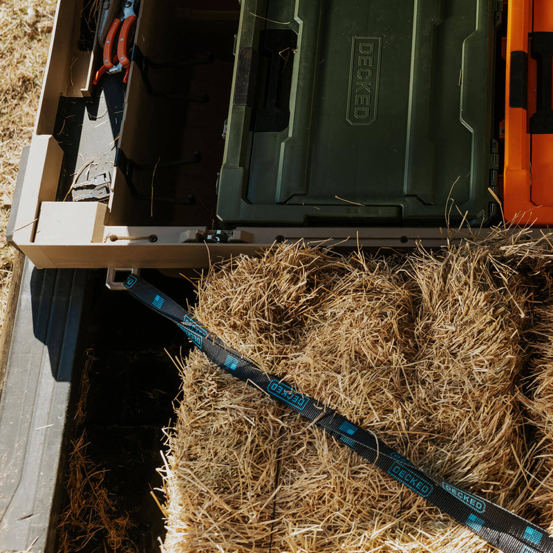 DECKED strap running from an aluminum tie down anchor on a DECKED Tool Box across straw bales loaded in the truck bed