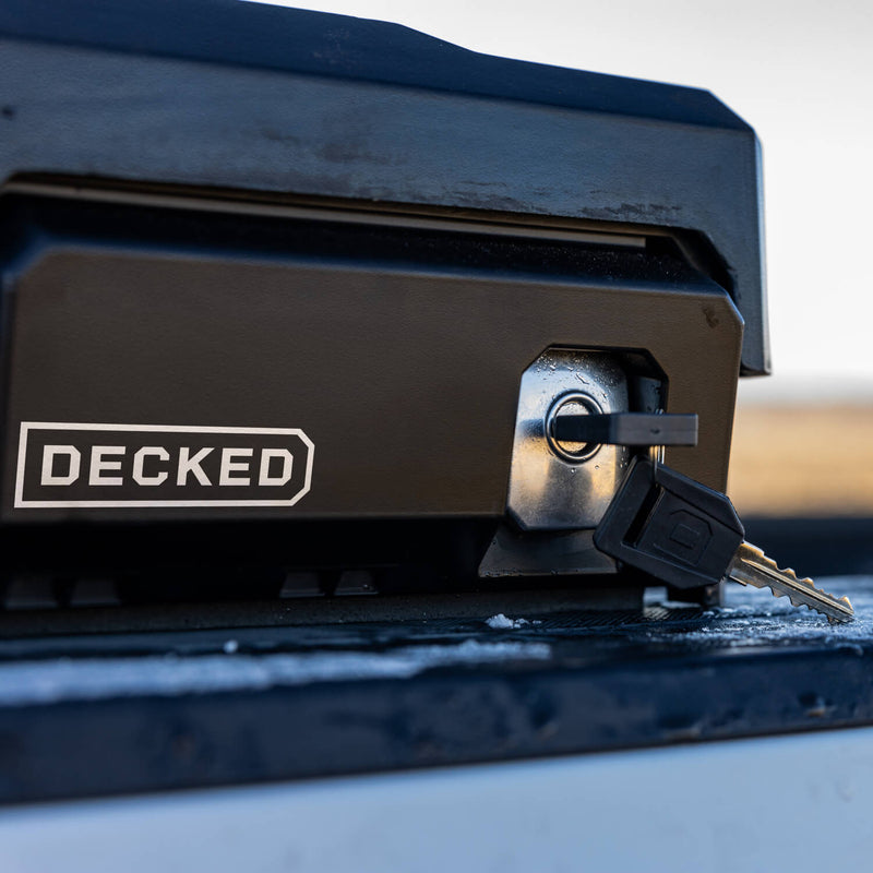 Close-up of the stainless armored lock and key on the black DECKED Tool Box, wet with rain