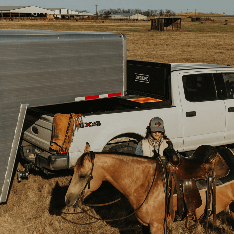 Black DECKED Tool Box open in a white Ford Super Duty at a ranch, with a saddled horse standing beside the truck