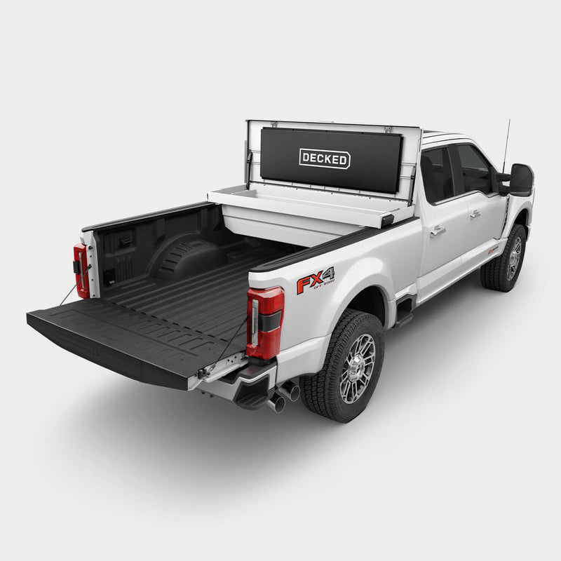 Industrial White DECKED Tool Box mounted crossbed behind the cab of a white Ford Super Duty, lid open, showing the mounting position and the bed space that stays free behind it