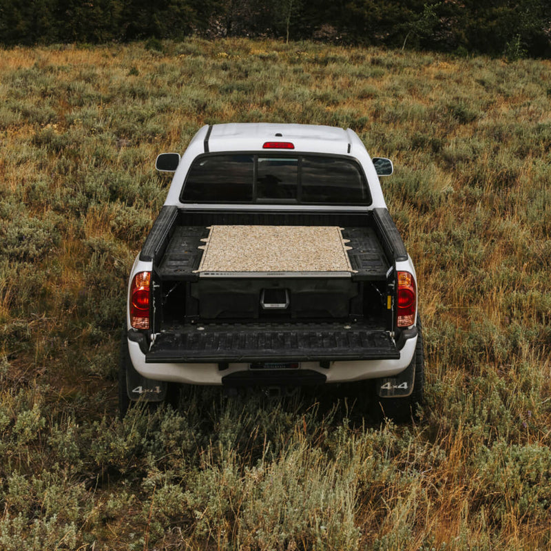 Tan camo DECKED Traction Mat installed on a midsize DECKED Drawer System deck in a white Toyota Tacoma, tailgate down