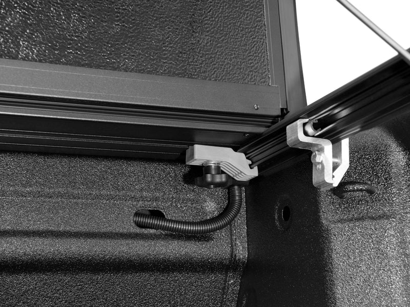 Close-up of the Flex drain tube and clamp at the front corner of the bed with the cover raised above.