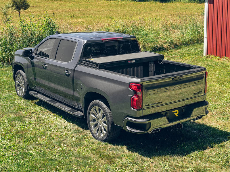 Hard folding tonneau cover with the rear panel folded forward on a pickup parked on grass