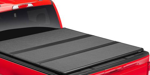 Closed hard tri-fold tonneau cover with three matte panels over a red pickup bed, rear three-quarter close-up