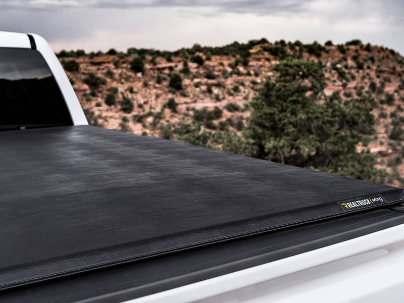 Close view of a soft tonneau cover stretched flat over a white pickup bed with scrubland behind