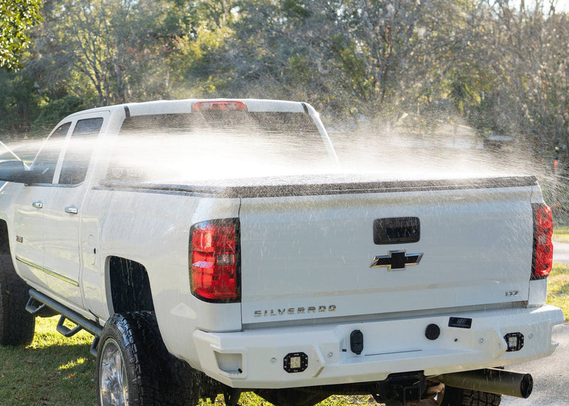 Water spraying across a closed soft tonneau cover on a white pickup outdoors