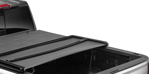 Soft tri-fold tonneau cover with the rear section folded forward over an open pickup bed, rear three-quarter close-up