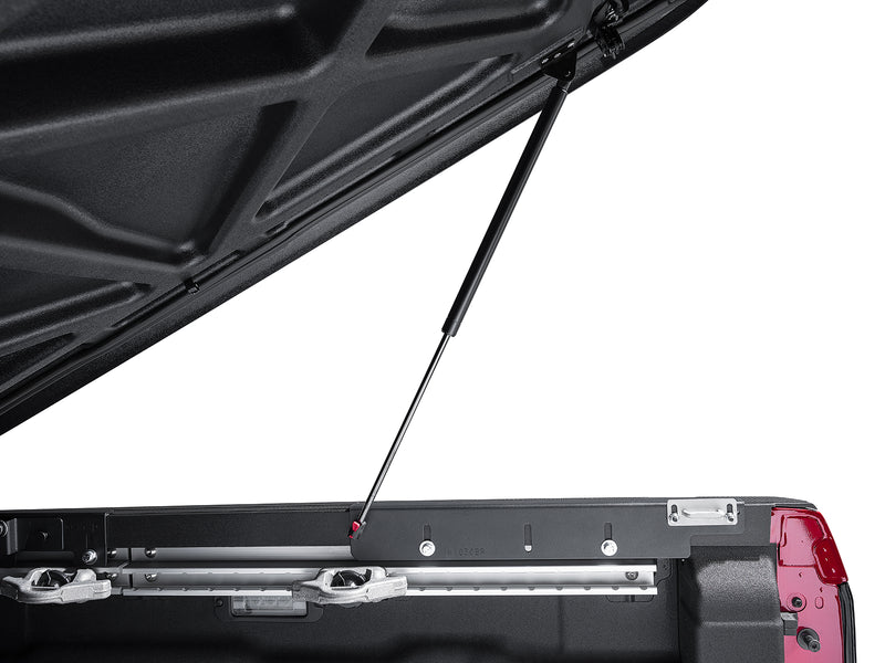 Close-up of the gas strut holding the Elite lid open above the bed rail, with the molded part stamp on the strut bracket.