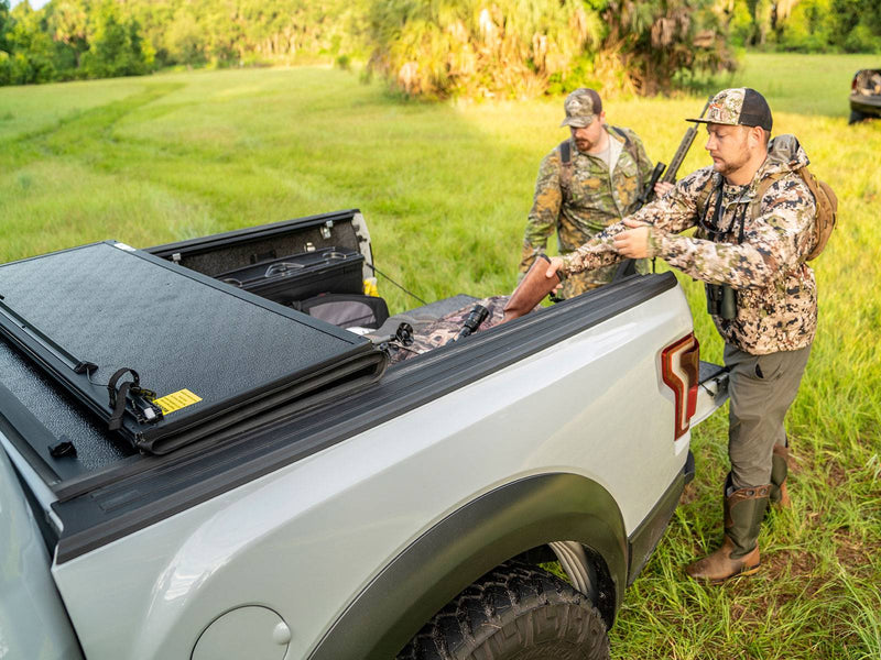 Gator EFX hard folding tonneau cover: Two hunters load gear beside a silver off-road pickup with its hard folding cover partly folded