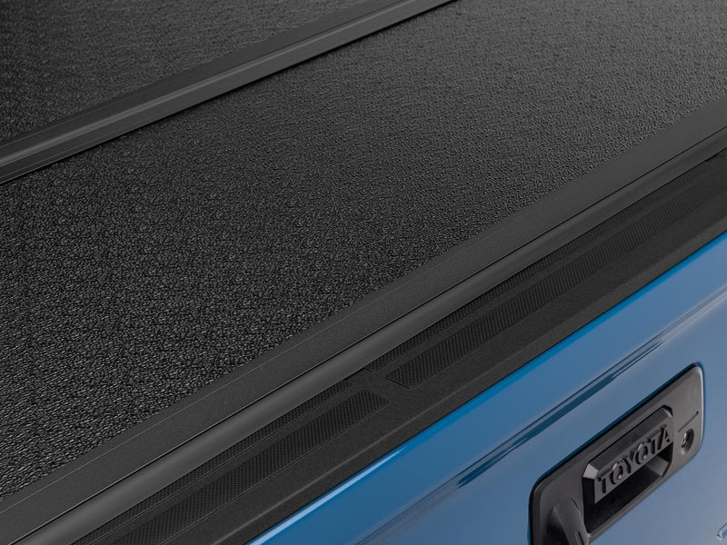Gator EFX hard folding tonneau cover: Close-up of the textured black hard cover panel closed over a blue tailgate with a Toyota handle bezel