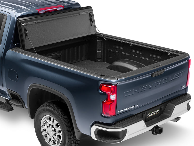 Gator FX hard folding tonneau cover: all panels folded and propped upright against the cab of a blue Chevrolet heavy-duty pickup