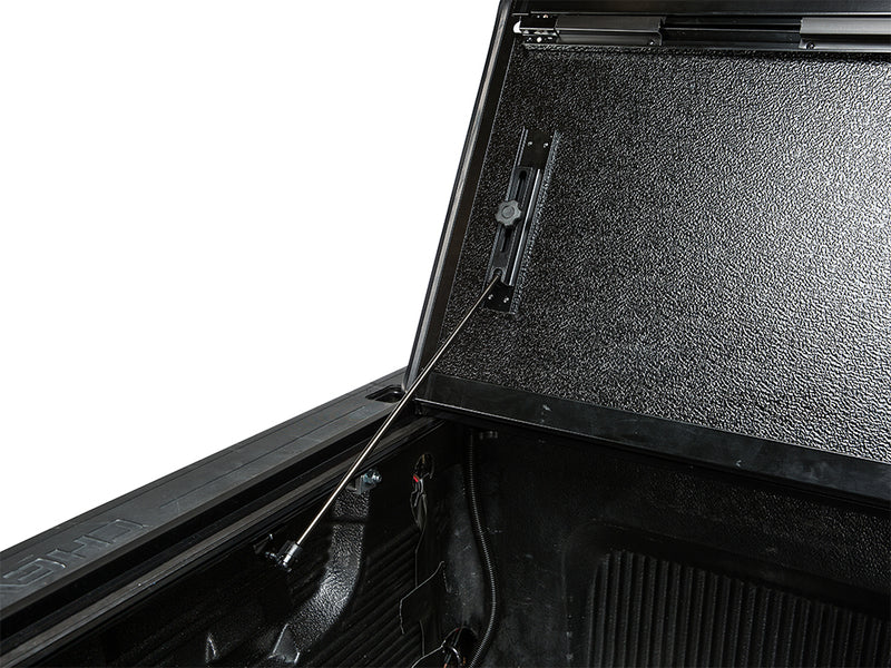 Close-up of the Gator FX tonneau cover: close-up of the underside of raised hard folding cover panels held up by a prop rod over a dark truck bed