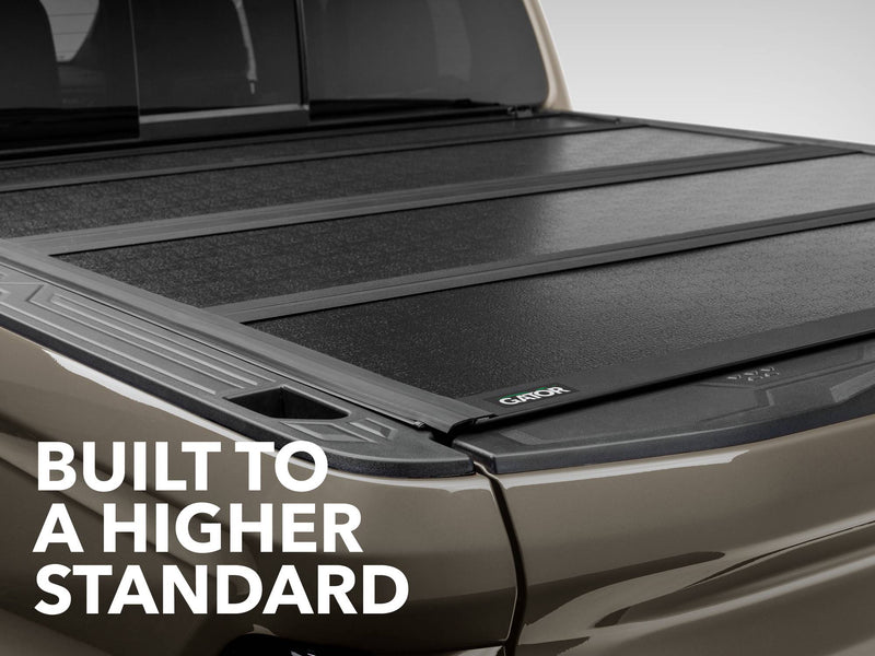Gator FX tonneau cover (closed) on a pickup bed: closed hard folding cover panels on a tan truck bed, captioned Built to a Higher Standard