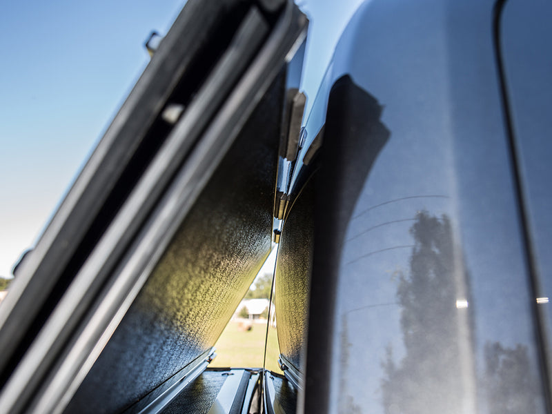Close-up of the Gator FX tonneau cover: folded hard cover panels stand upright against the cab of a glossy dark truck outdoors