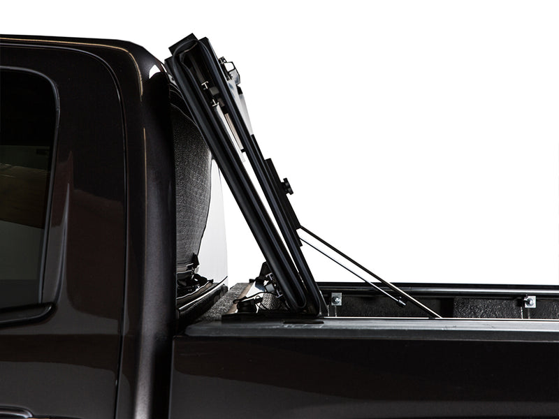 Gator FX tonneau cover (upright) on a pickup bed: side close-up of a hard folding cover stacked upright and propped against the cab of a black truck