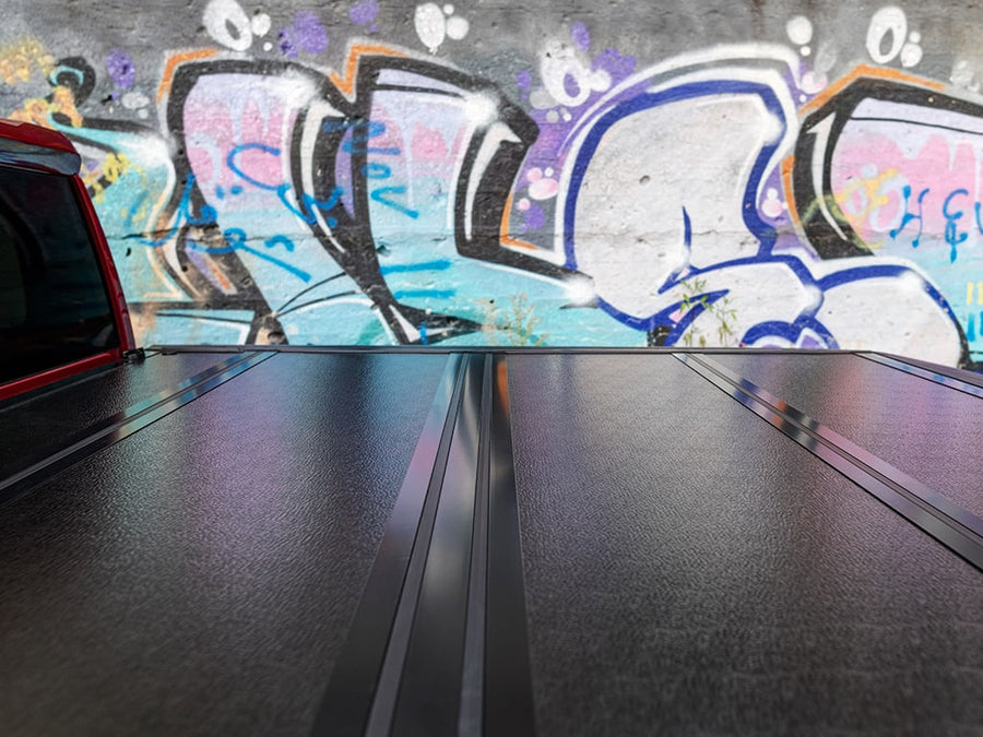 Gator FX Hard Folding tonneau cover: Low view across the closed black hard panels of a folding tonneau cover in front of a graffiti wall.