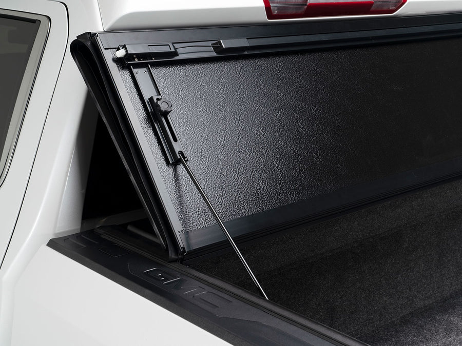 Gator FX Hard Folding tonneau cover: A hard folding tonneau cover stands upright against the cab of a white truck with its prop rod extended.
