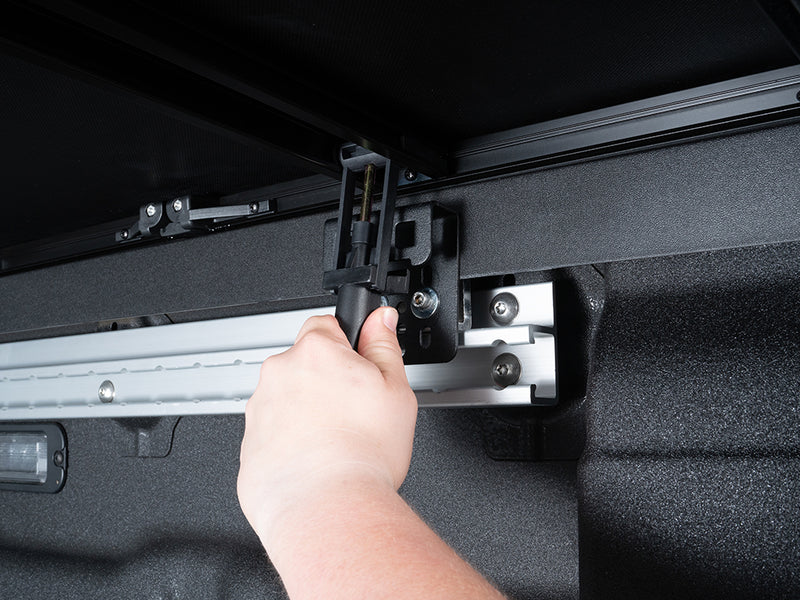 Close-up of the Gator SFX tonneau cover: A hand tightens a clamp holding the cover rail inside a bed with a spray-in liner