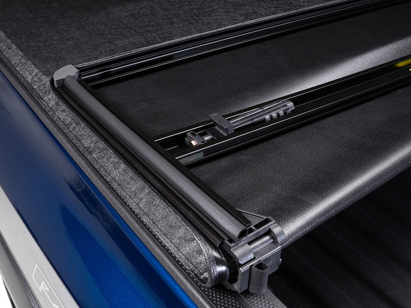 Close-up of the Gator SFX tonneau cover: close-up of the frame cross bar and latch beside the folded vinyl on a blue truck