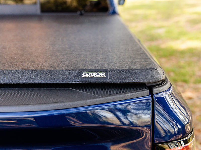 Close-up of the Gator SFX tonneau cover: rear corner of the closed soft cover with the Gator logo tag on a blue truck outdoors