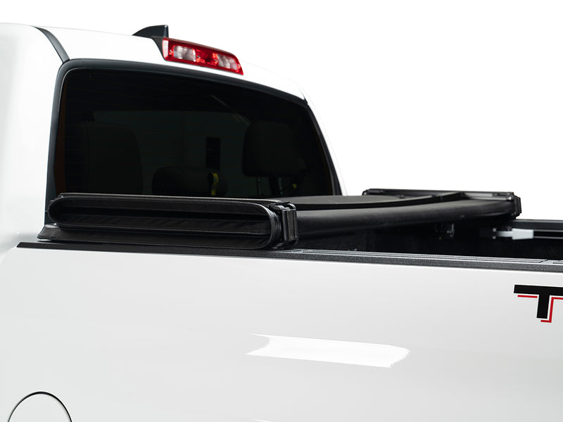 Gator SFX soft tri-fold tonneau cover: folded cover strapped up behind the cab of a white Toyota pickup, close-up