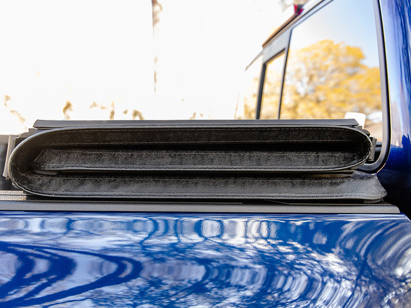 Gator SFX soft tri-fold tonneau cover: folded and strapped against the cab of a blue pickup, close-up