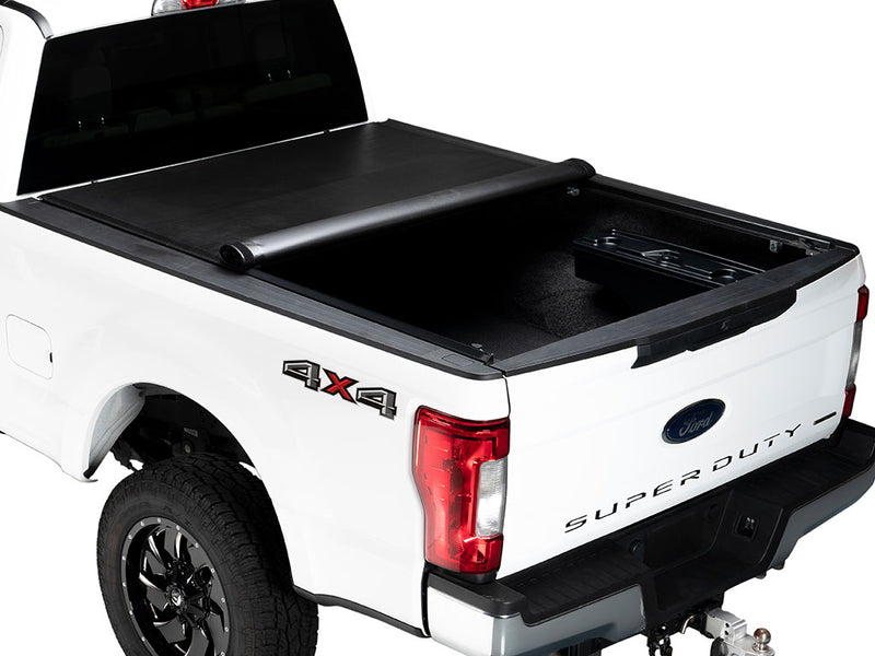 Gator SRX soft roll-up tonneau cover: A white Ford Super Duty pickup with the soft roll-up cover partly rolled toward the cab, showing a storage tray in the bed