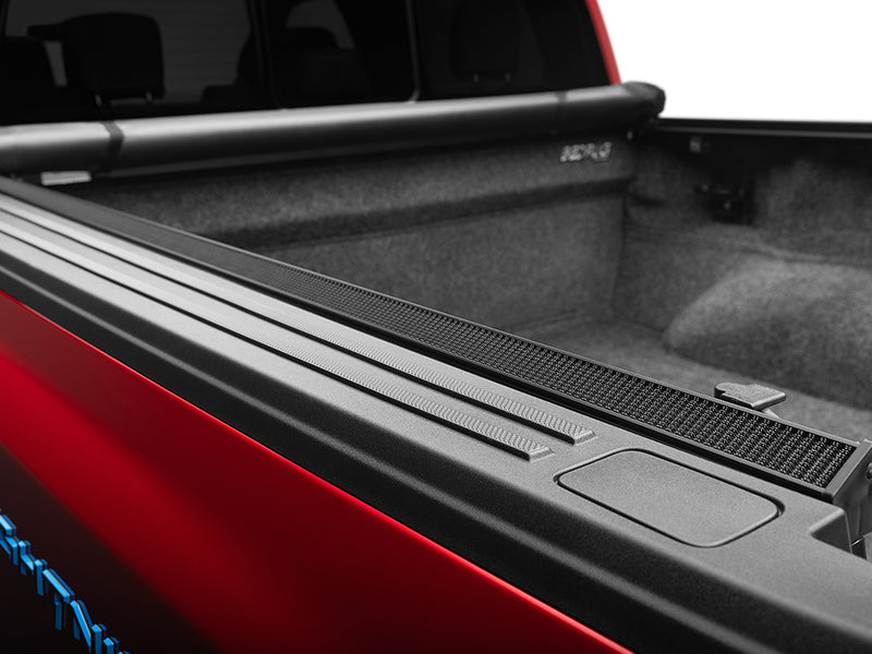 Gator SRX tonneau cover (open) on a pickup bed: the soft cover rolled up at the cab of a red pickup, with the side rail running along a carpeted bed