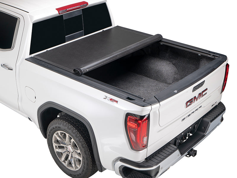 Gator SRX soft roll-up tonneau cover: White GMC Sierra with a soft roll-up tonneau cover half rolled, showing a carpeted bed liner
