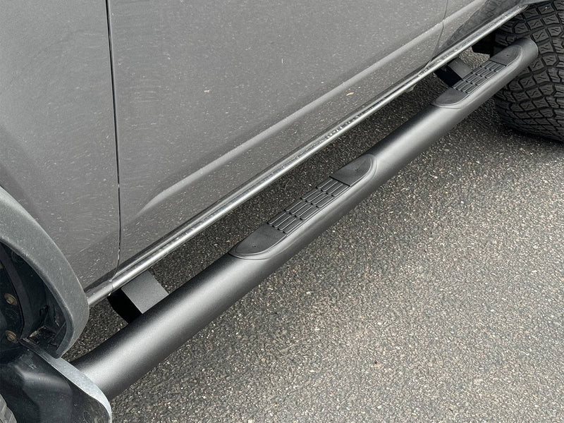 Go Rhino 4000 Series: black round side step with molded step pads mounted below the doors of a gray SUV, parked on asphalt