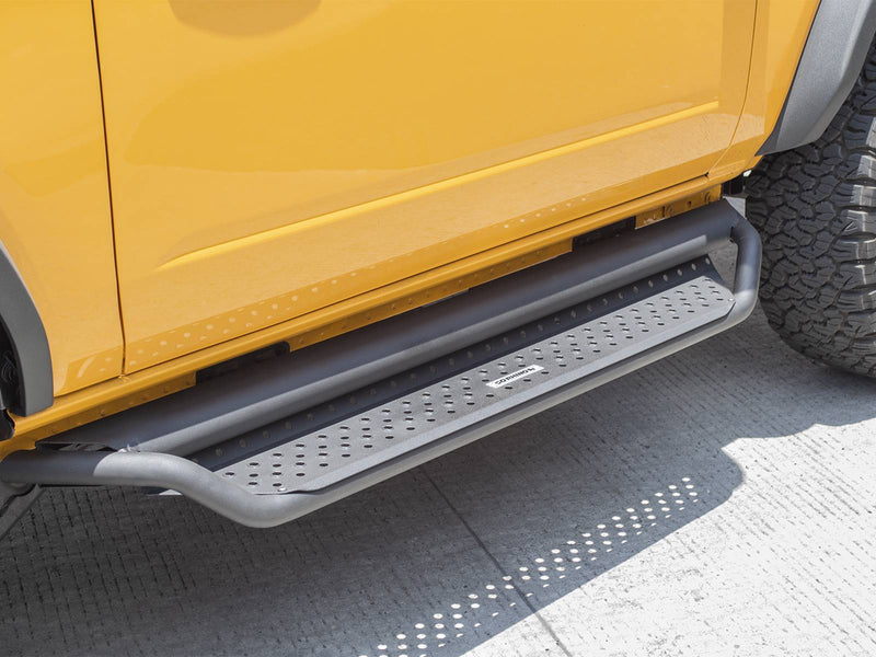 Go Rhino Dominator D1: dark textured side step with perforated tread mounted under the door of a yellow SUV, parked on concrete