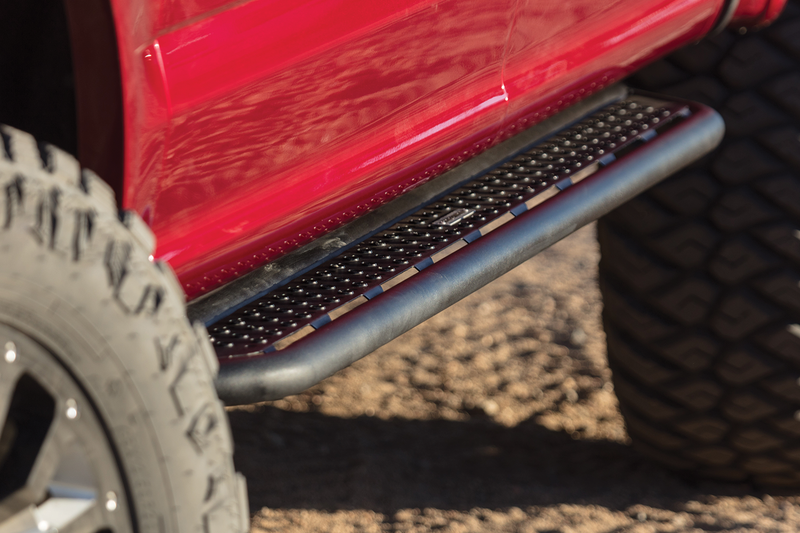 Go Rhino Dominator D6: black tube-rail step with perforated plate installed under a red truck door between off-road tires (shown with aftermarket wheels and tires, not included)