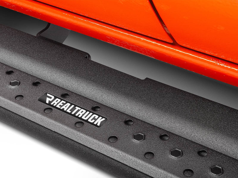 Go Rhino Dominator DSS: close-up of a black textured slider board with RealTruck badge plate below an orange vehicle body