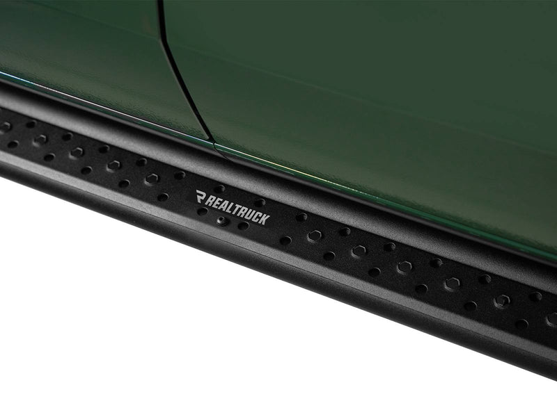 Go Rhino Dominator DSS: close-up of a black textured slider board with RealTruck badge plate mounted below a dark green door