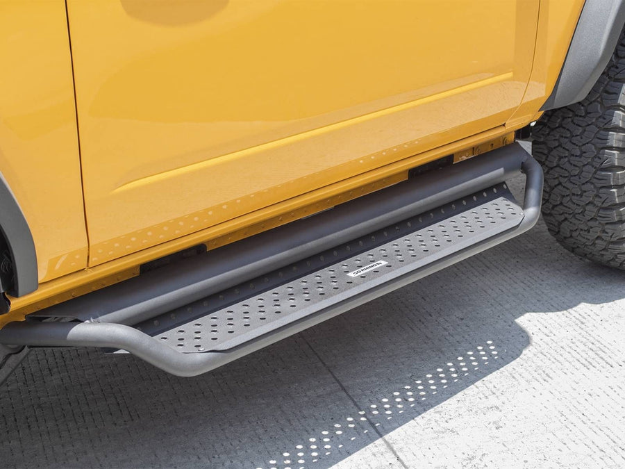 Go Rhino Dominator D1 Side Steps: Dark textured side step with perforated tread mounted under the door of a yellow SUV, parked on concrete