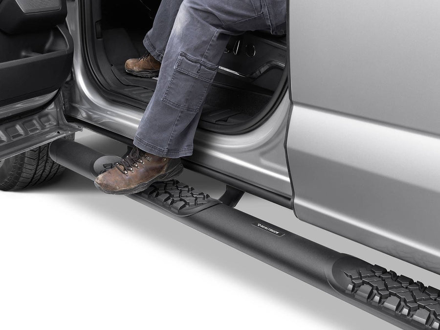 Go Rhino V-Series V3 Side Steps: Work boot on the tread pad of a black side step under the open door of a silver pickup
