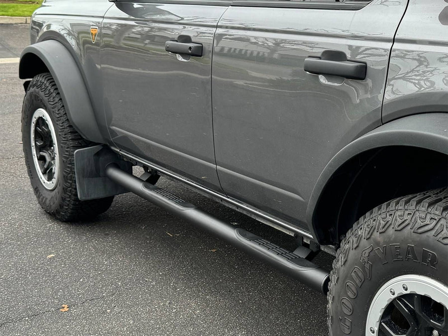 Go Rhino 4000 Series Nerf Bars: Black round side step with step pads below the doors of a gray 4-door SUV with flared fenders, parked on asphalt