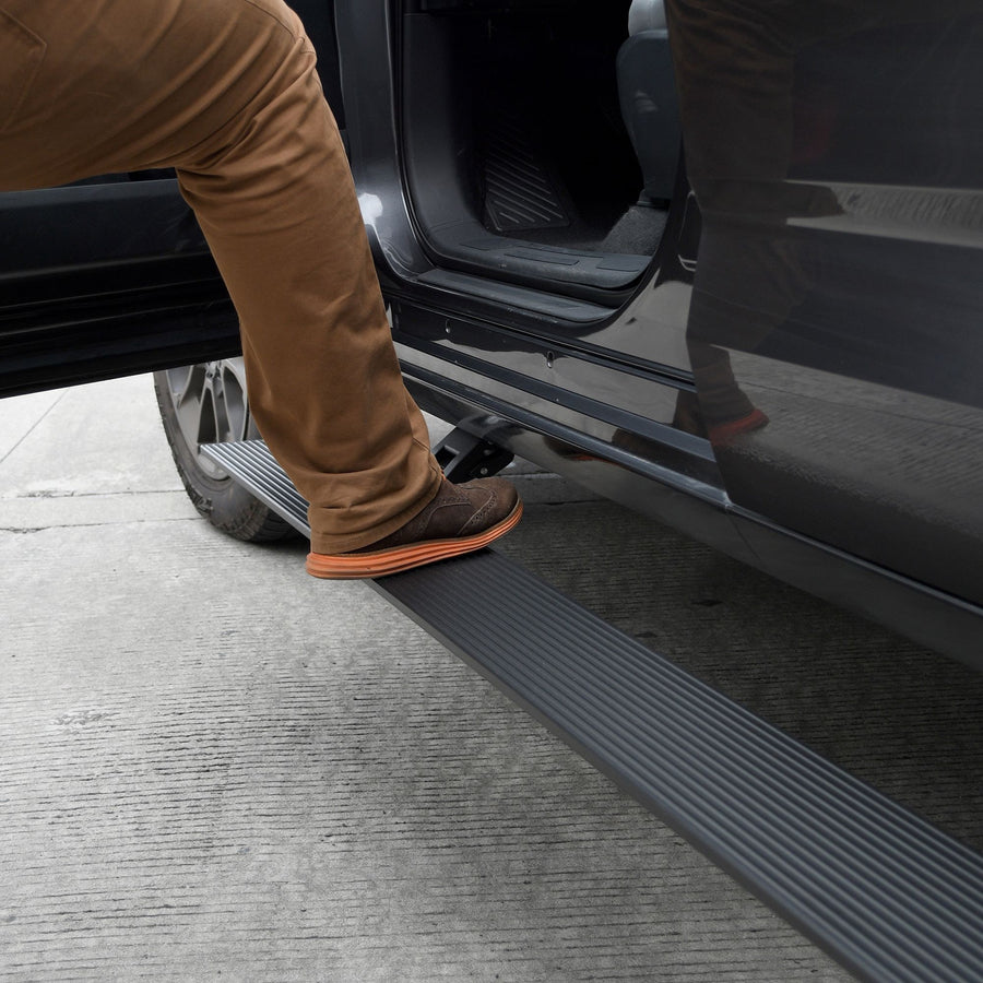 Go Rhino VoltStep Electric Running Boards: Black ribbed power running board deployed under the open front door of a dark gray vehicle, a person stepping on it